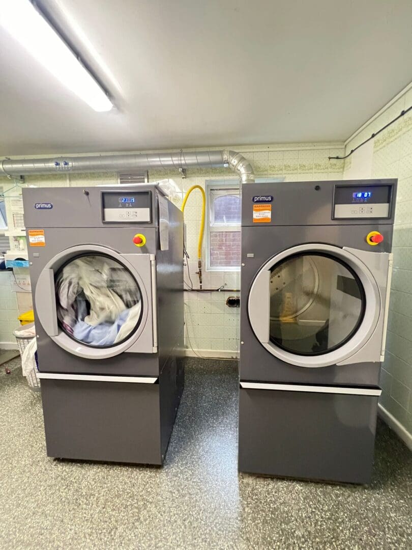 Two industrial washing machines in laundry room.